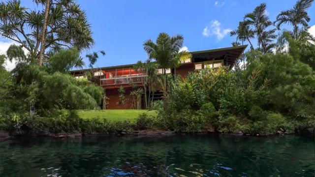 A beautiful riverfront house surrounded by lush greenery, reflecting in the calm waters of the river. Perfect for those seeking tranquility and a close connection with nature, ideal for Kauai vacation rentals. Serene River View Surrounded by Lush Greenery